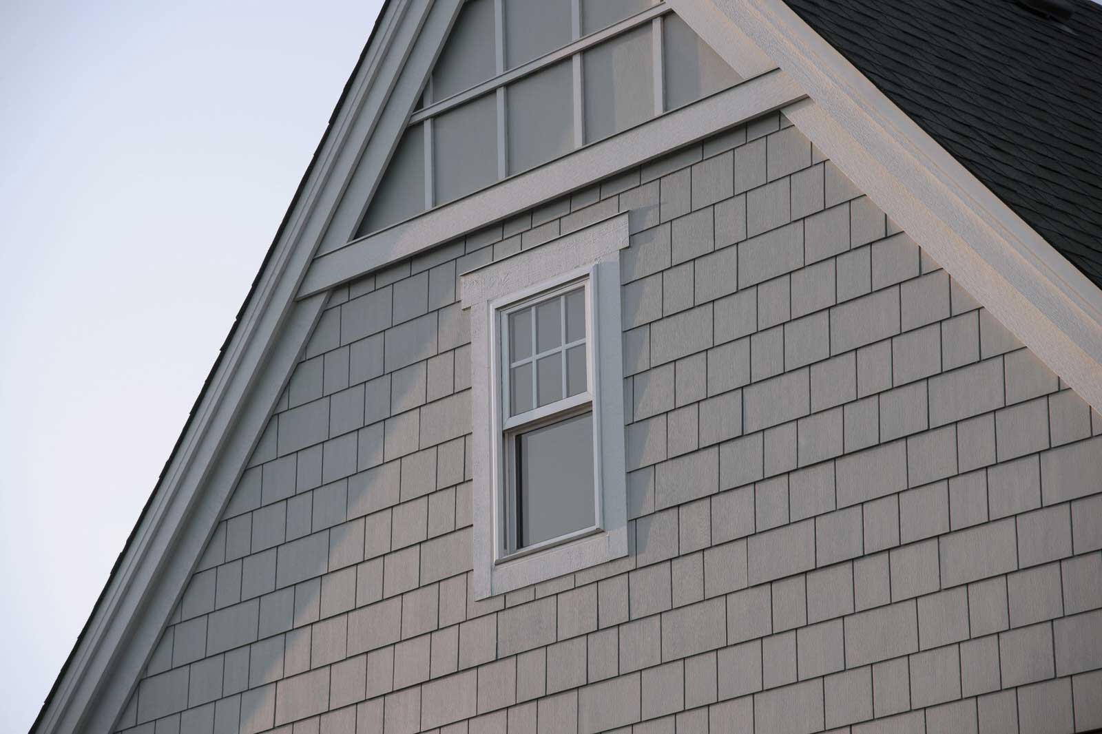 Close-up of a gray shingled house wall with a small white-framed window near the roofline