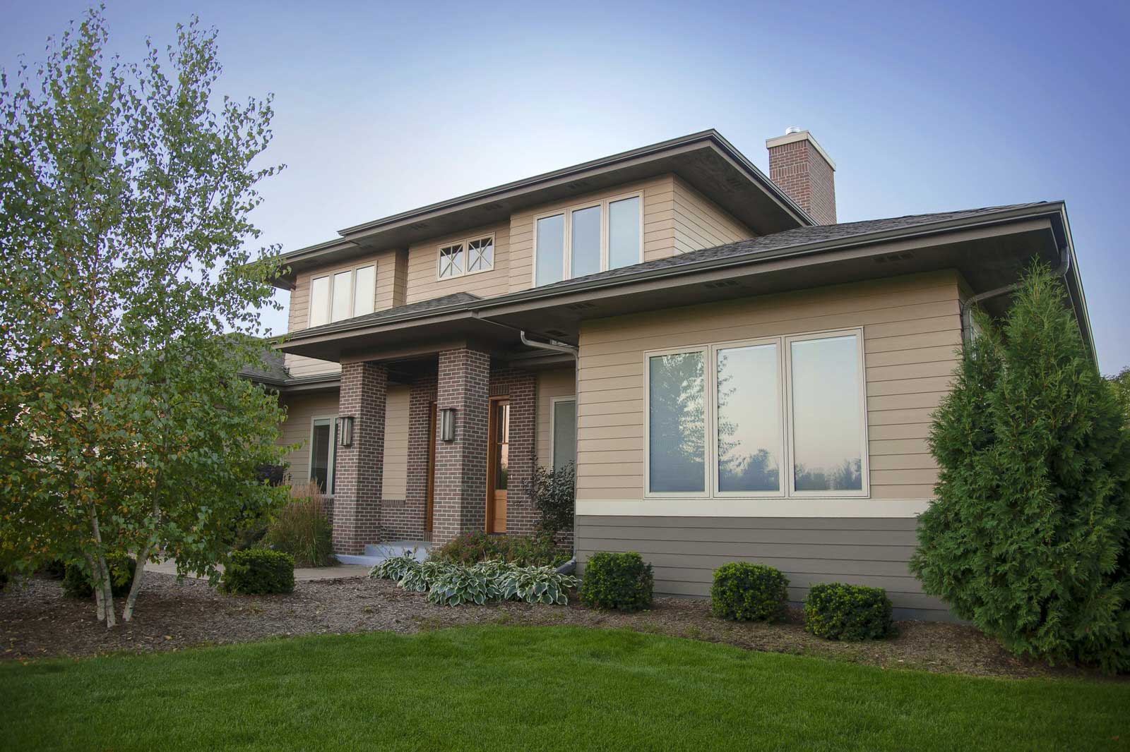 Two-story suburban house with brick and beige siding, front porch, large windows, and a landscaped yard