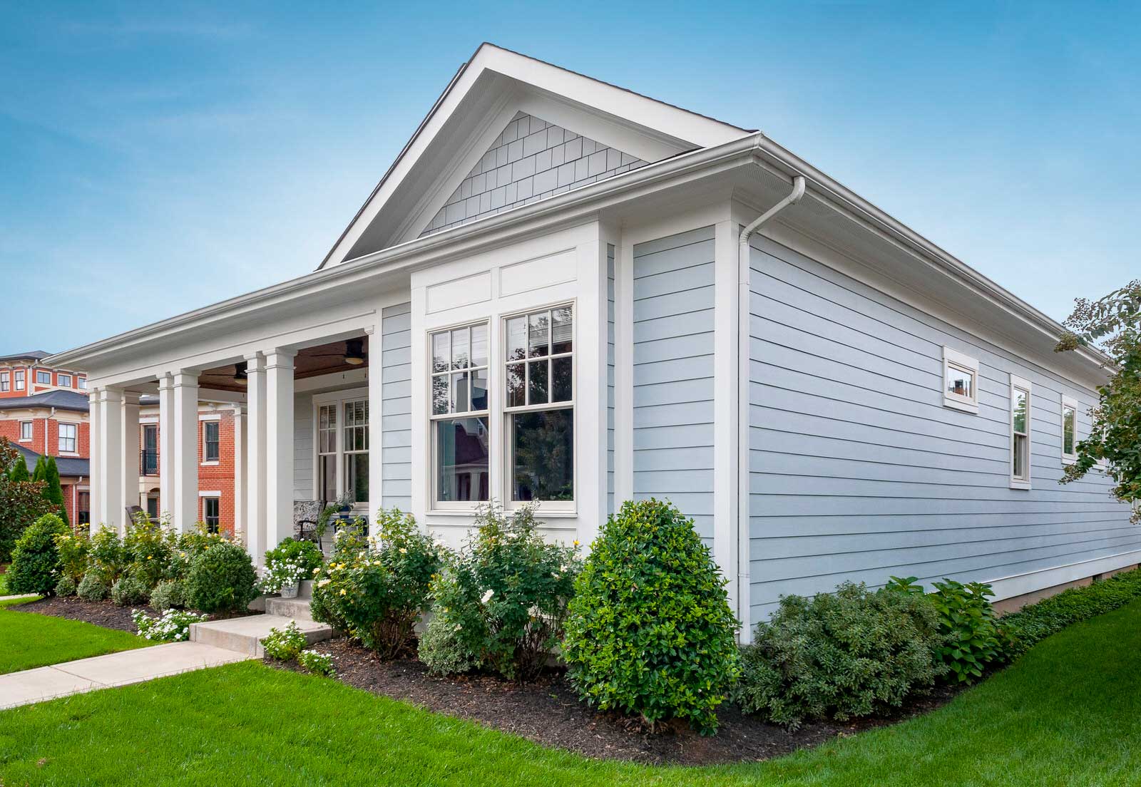 White craftsman-style house with a front porch, white siding, and green lawn under a blue sky