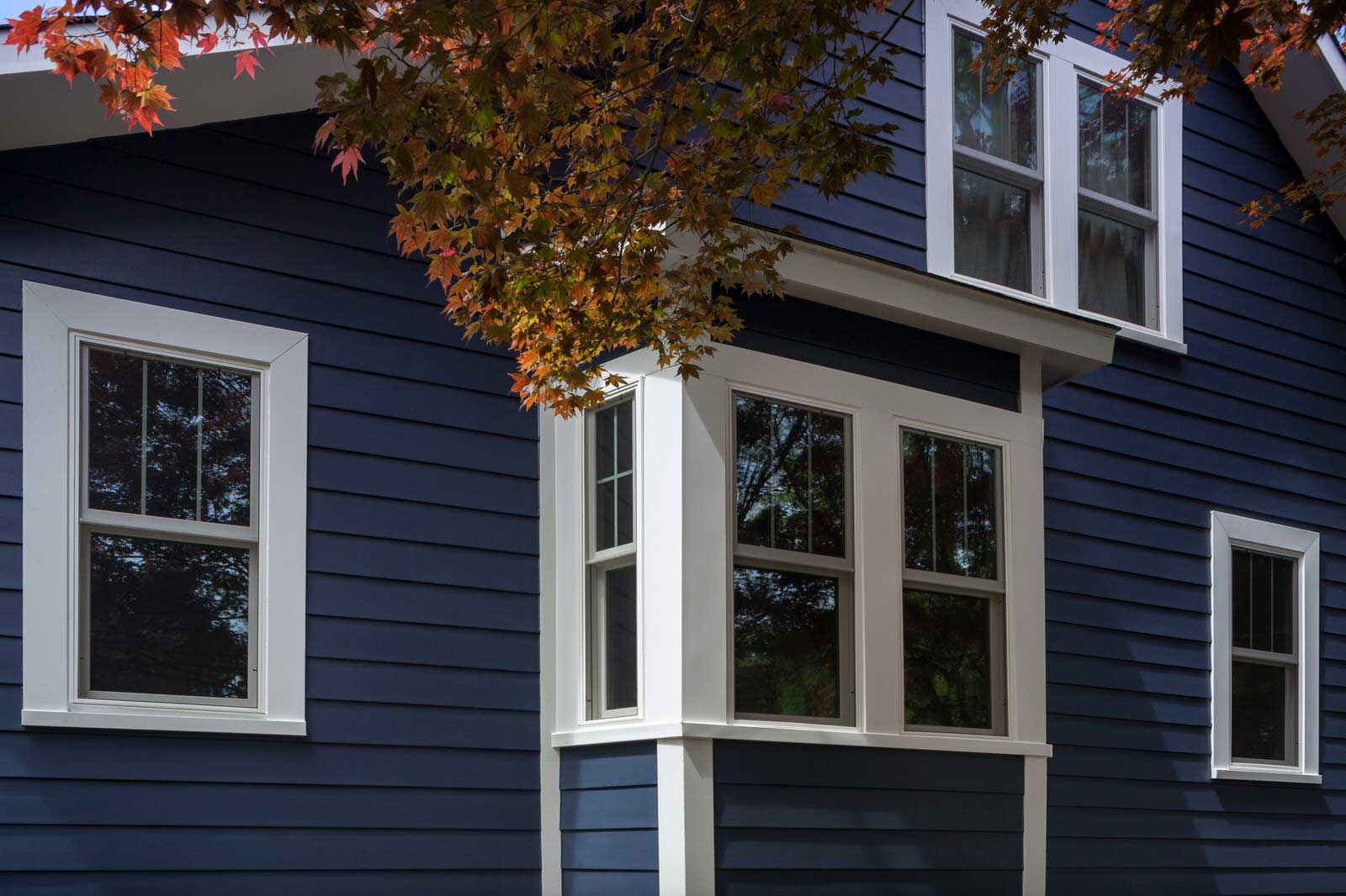 Blue house exterior with white-trimmed windows and autumn leaves overhead