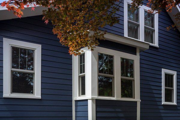 Blue house exterior with white-trimmed windows and autumn leaves overhead
