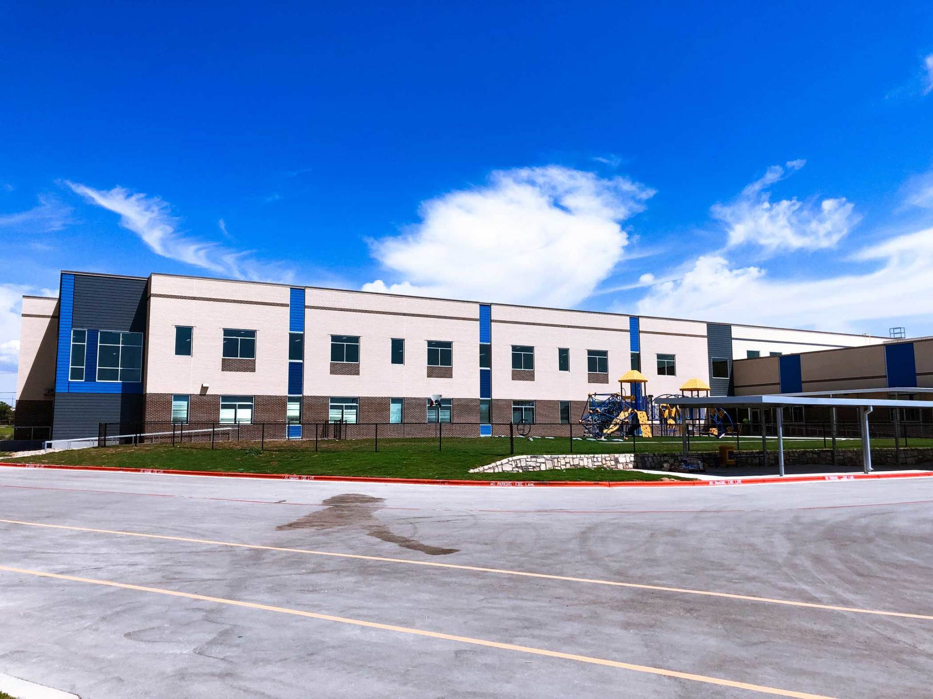Modern two-story building with white and blue facade under a bright blue sky, seen from the parking lot