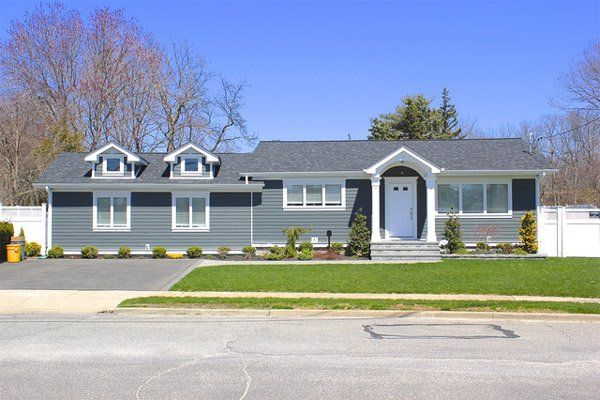 Single-story gray house with white trim and a front lawn on a sunny street