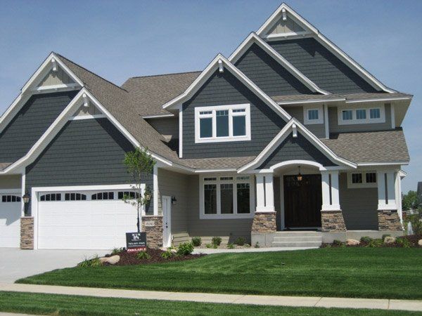 Large gray suburban house with gabled roofs, white trim, a two-car garage, and a manicured lawn