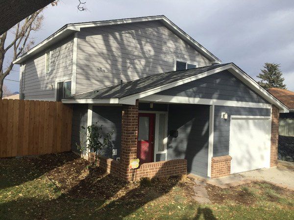 Two-story gray house with white garage, red front door, and wooden fence in the yard