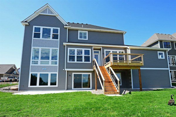 Blue-gray house with large windows, backyard deck, and wooden stairs on a green lawn