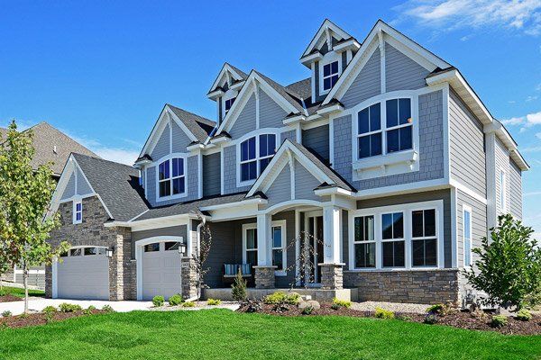 Modern gray two-story suburban house with white trim, stone accents, and a green lawn