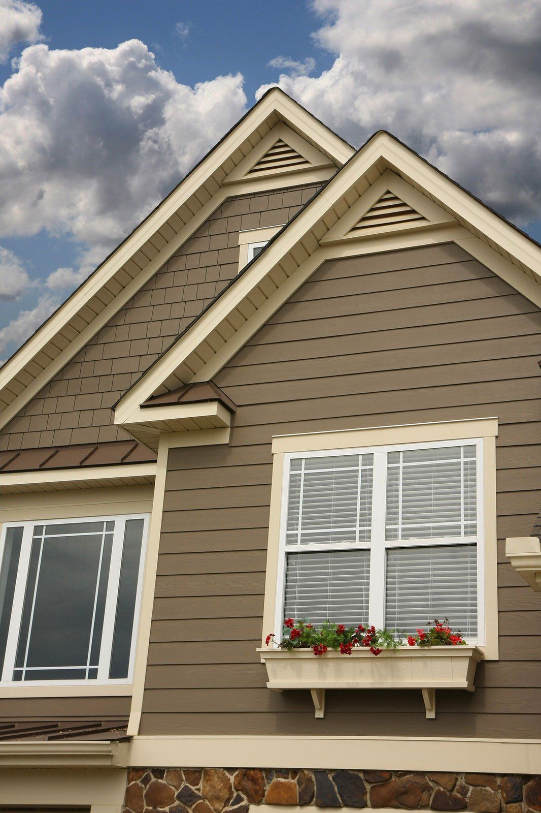House exterior with beige siding, white-trim windows, and flower box beneath a cloudy sky