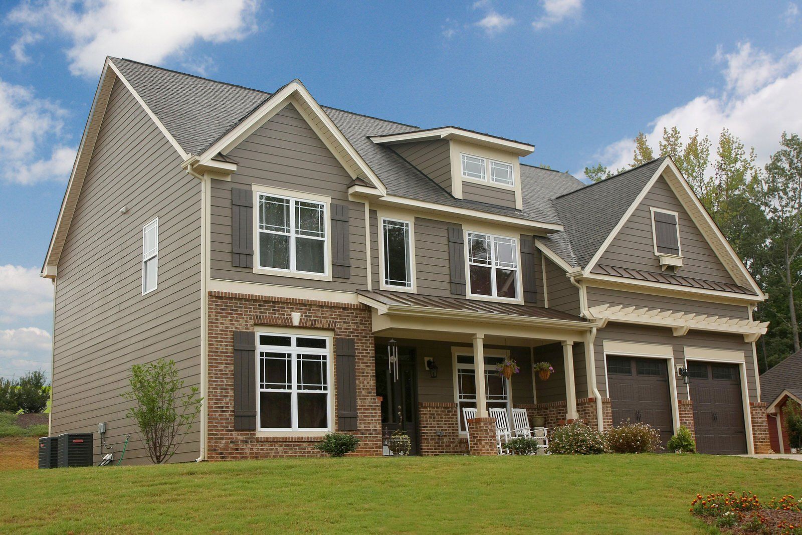 Large two-story suburban house with gray siding, white trim, and a stone porch under a blue sky