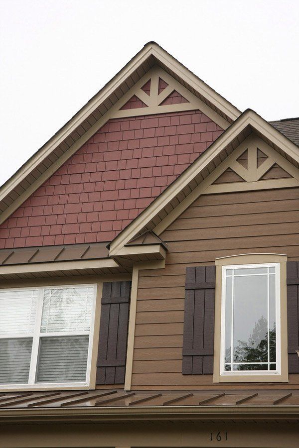 Two-story house exterior with tan siding, maroon shingle gables, and white-framed windows