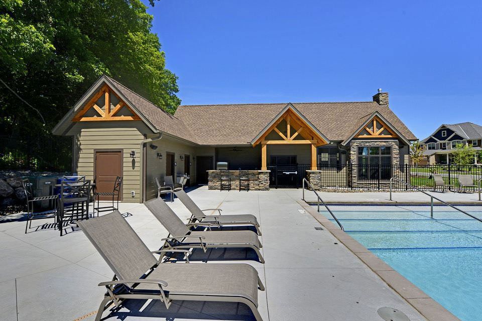 Outdoor pool with lounge chairs beside a tan clubhouse under a blue sky