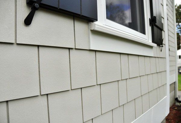 Close-up of gray house siding with a white-trimmed window and black shutters