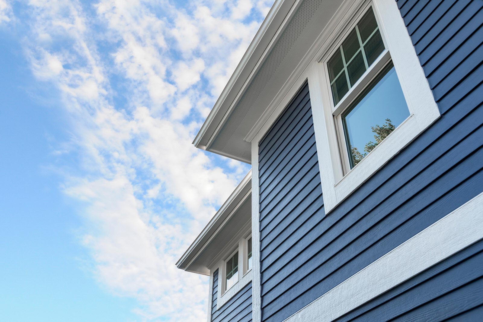 Blue house exterior with white-trimmed windows against a cloudy sky
