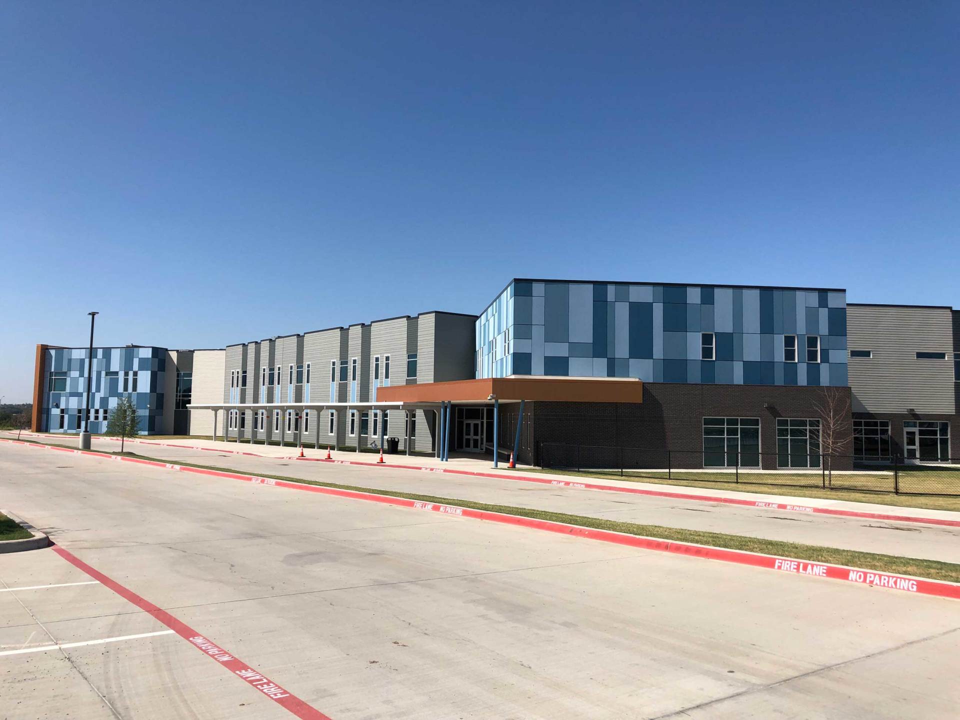 Modern blue-and-gray commercial building with a long driveway under a clear sky