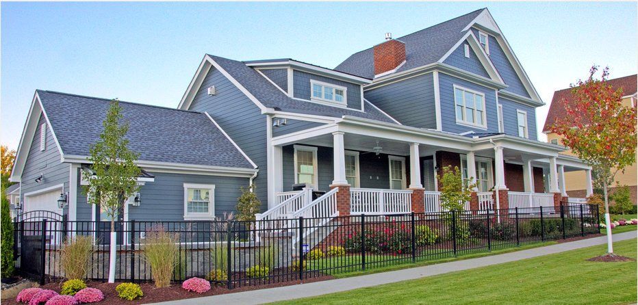 Blue Victorian-style house with white trim, front porch, and colorful flower beds behind a black iron fence