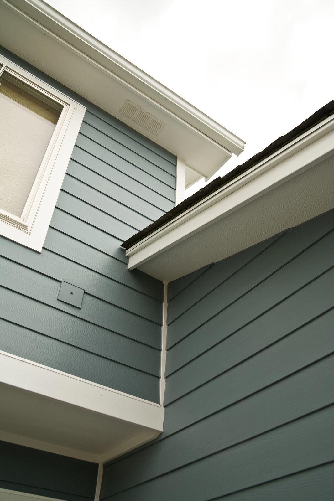 Blue-gray house siding and eaves meeting at an exterior corner under a bright sky.