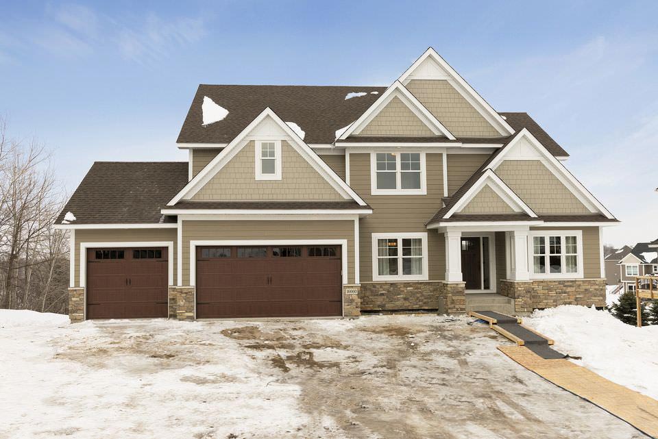 Large beige suburban house with two garages and a snowy driveway