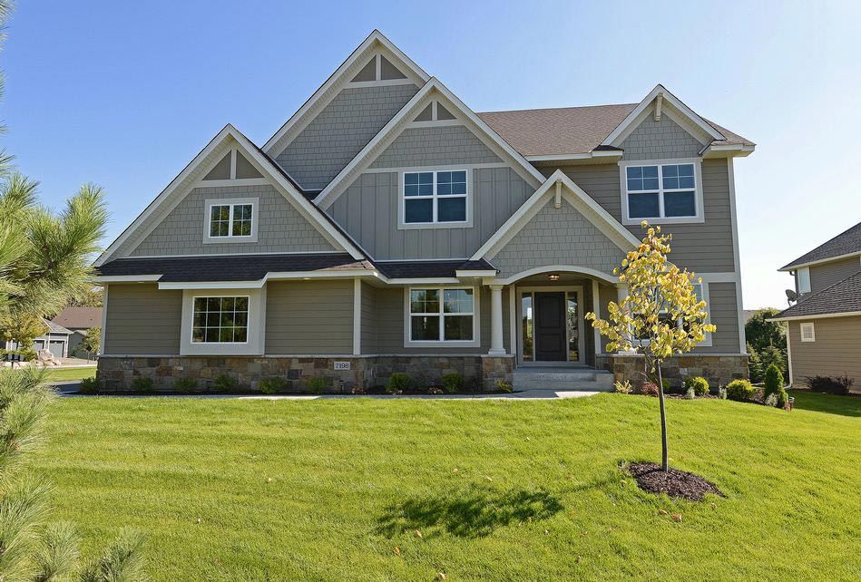 Large gray suburban house with a manicured lawn and a small tree in front