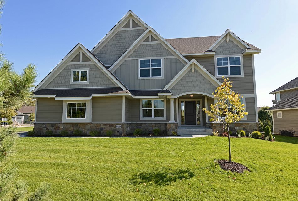 Two-story suburban house with gray siding, front lawn, and a small tree under a blue sky