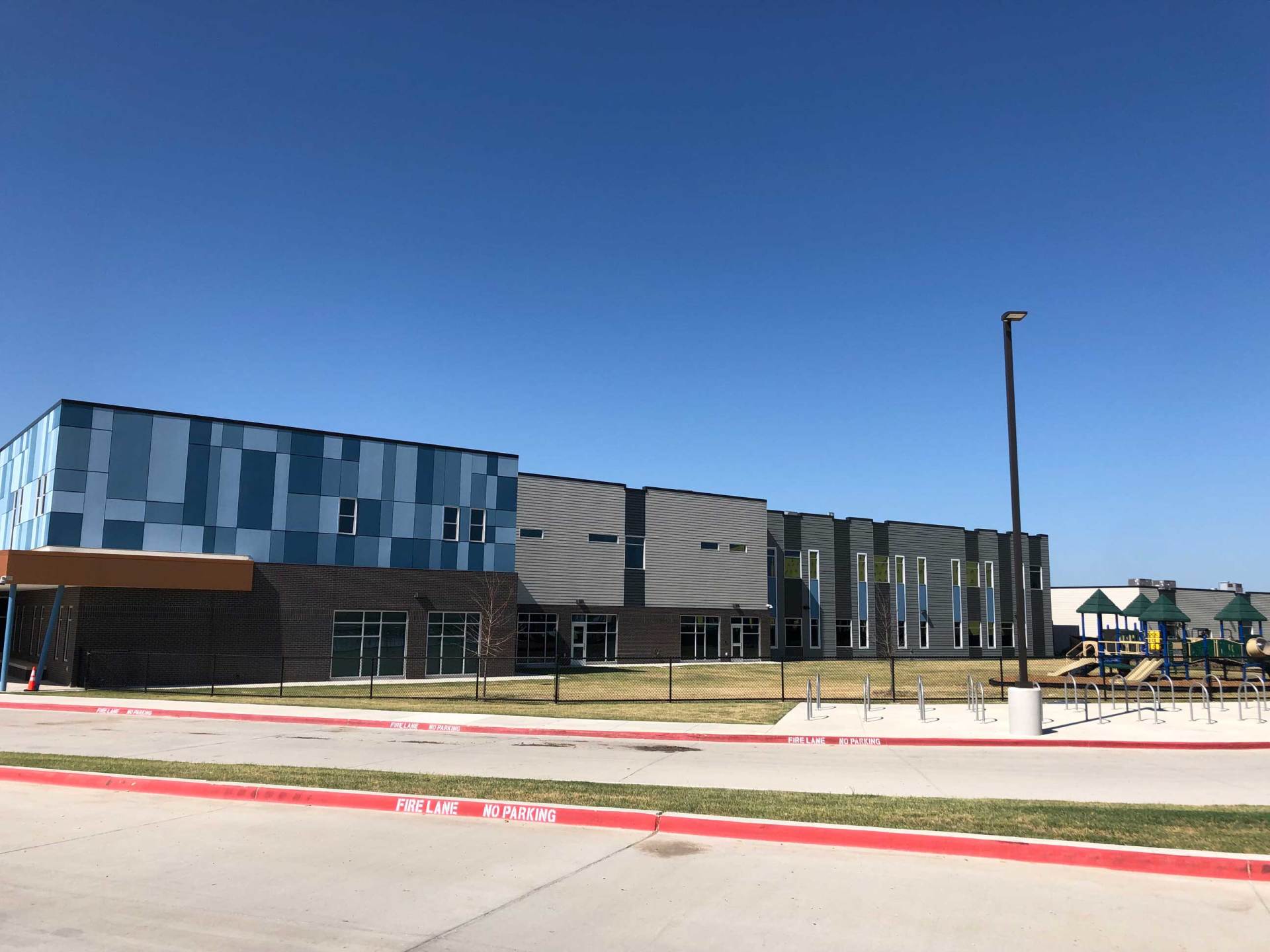Modern school building with blue and gray panels under a clear sky, viewed from a street corner