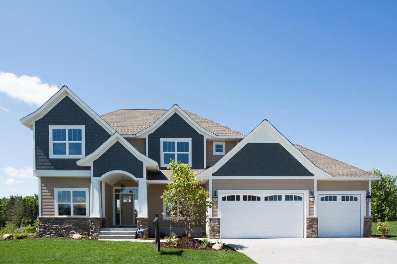 Modern two-story suburban house with gray siding, white trim, and a three-car garage under a blue sky