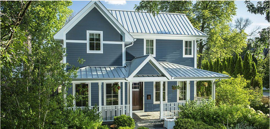 Blue two-story house with white trim, metal roof, and covered front porch surrounded by trees