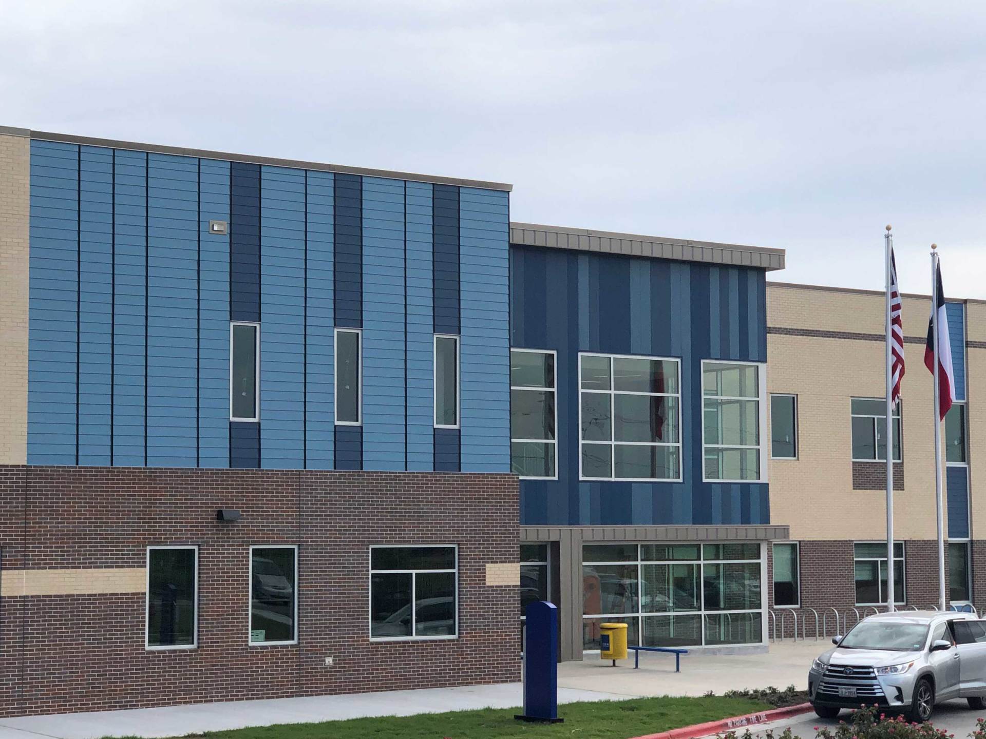 Modern blue-and-brick building exterior with flags and parked vehicles