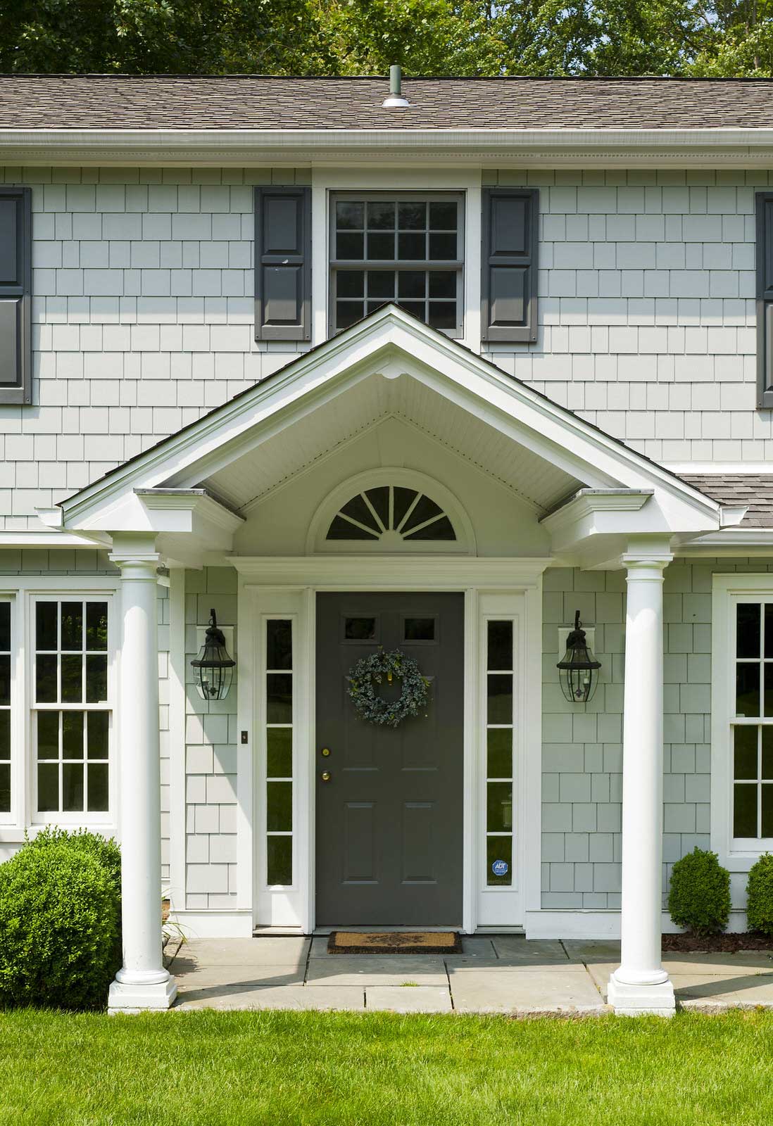 Front view of a white house with dark shutters, a gray door, and a columned porch.