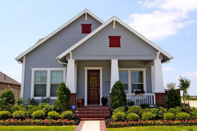 Gray single-story house with white trim, red accents, and a front porch bordered by manicured landscaping