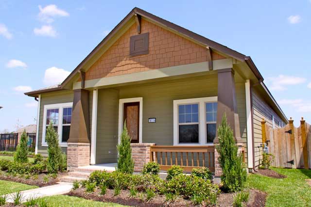 Small tan house with brown trim, front porch, and landscaped yard under a clear sky