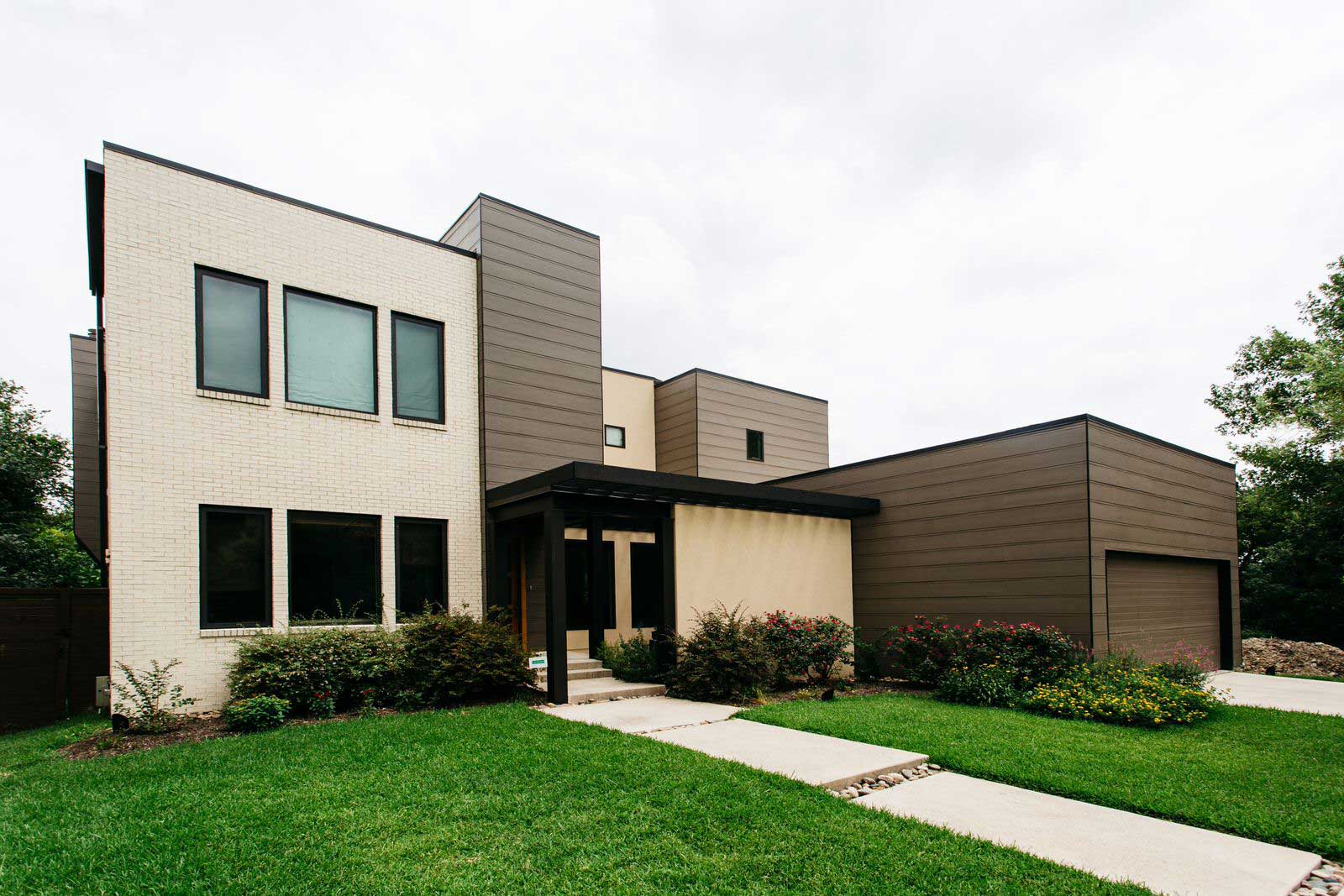 Modern two-story house with beige and white exterior, large windows, and a green lawn