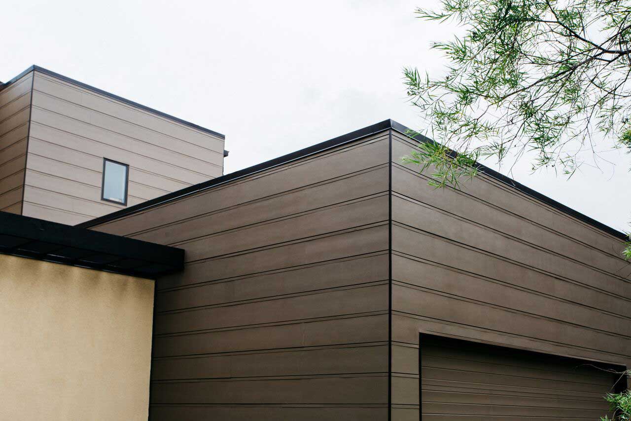 Modern brown house exterior with a garage and tan siding under an overcast sky