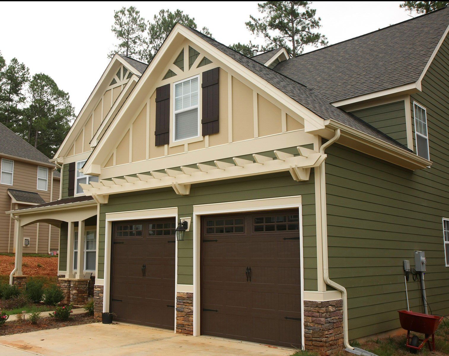 Two-story suburban house with tan siding, brown garage doors, and stone accents