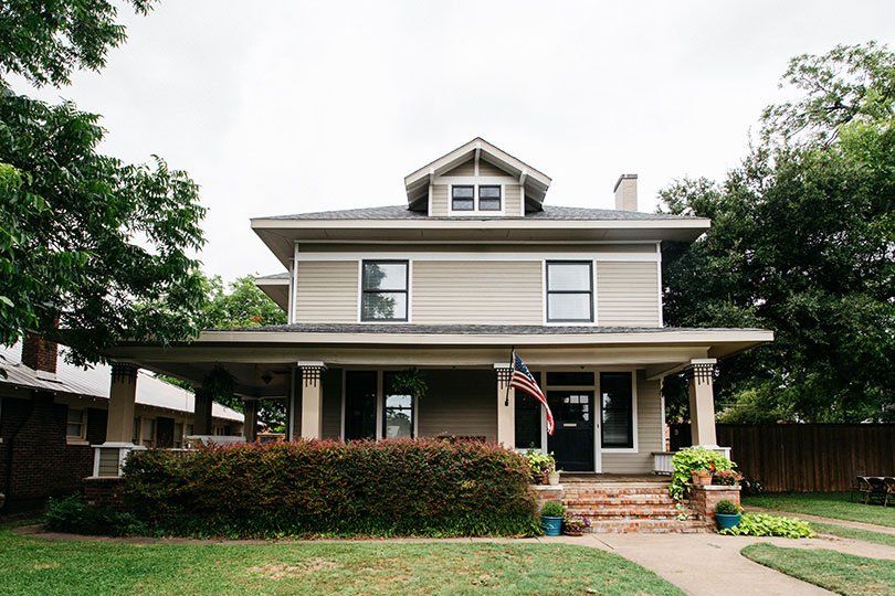 Two-story house with a front porch, white trim, and a small American flag in the yard.