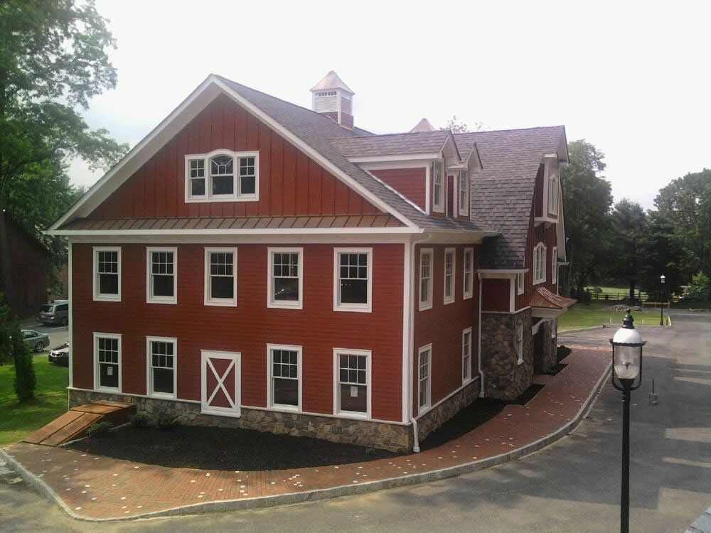 Red brick historic building with white trim and a stone base, seen from the corner by a paved drive.