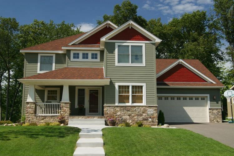 Two-story beige house with red roof, stone accents, and a white garage in a green front yard