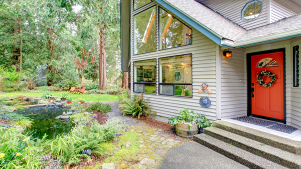 Picture of an orange front door in an entrance way to a house in a wooded area.