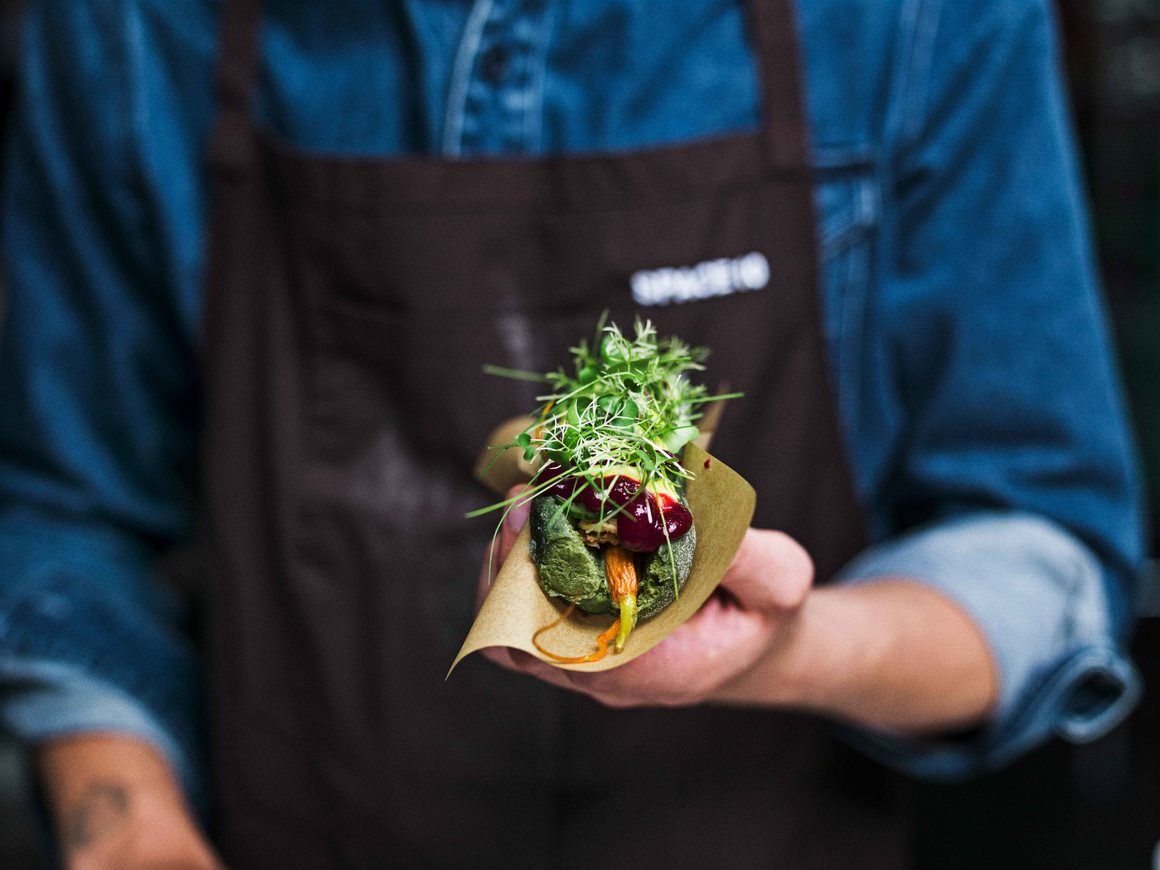 A meatless hotdog with ingredients that include spirulina, pickled mustard seeds & chives, a beetroot-black currant ketchup, curried mayo and garnished with crispy onions and micro-greens.