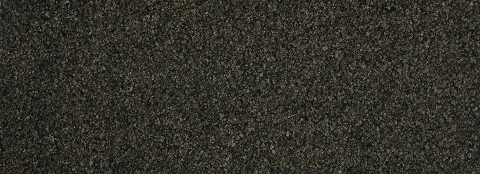 A close-up texture of dark, speckled, fine-grained material, appearing like asphalt or dark composite stone.