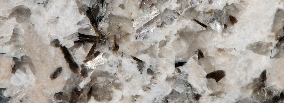 A close-up of a rock surface showing white, translucent crystals interspersed with dark, needle-like mineral inclusions.