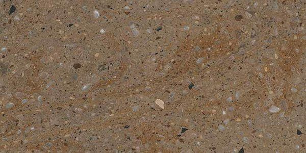 Close-up of a tan-colored, textured concrete or engineered stone surface with embedded small, dark, and light particles.