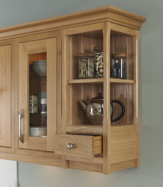 Light oak wooden kitchen wall cabinets featuring glass doors, open display shelves with jars, and a small pull-out drawer.