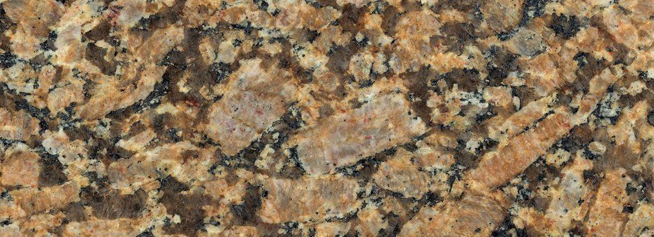 Close-up of a granite stone surface with a textured pattern of brown, tan, and black mineral flecks and crystals.