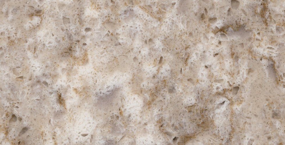 A close-up view of beige quartz countertop material featuring speckled, mottled patterns in cream and light brown tones.
