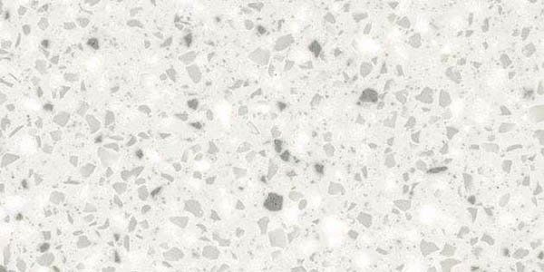 A close-up of a white granite or quartz countertop surface featuring small, scattered gray and white flecks and chips.