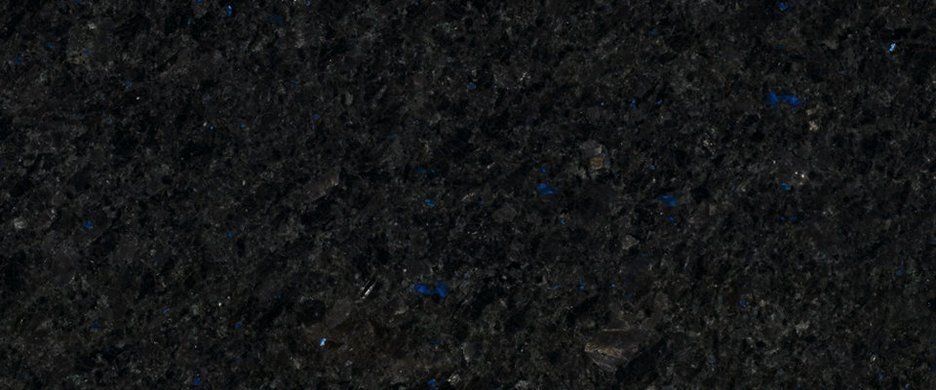 A close-up, textured view of dark, coarse soil or gravel with scattered tiny blue specks.