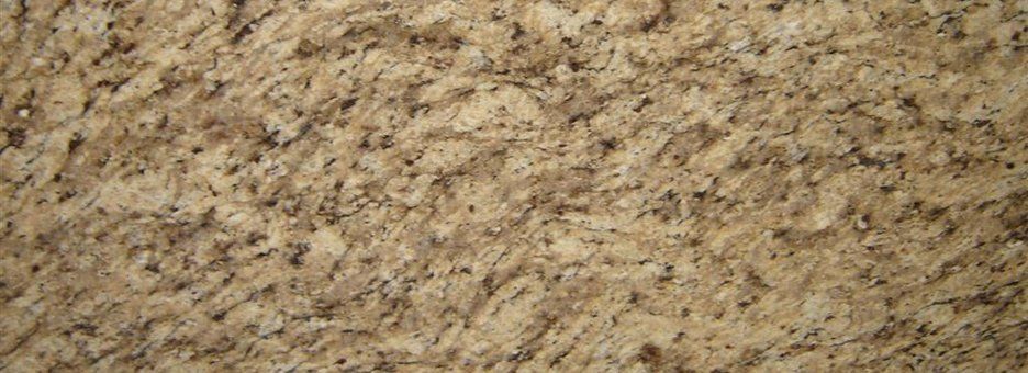 Close-up of a textured granite surface in shades of beige, cream, and tan with scattered dark brown and black flecks.