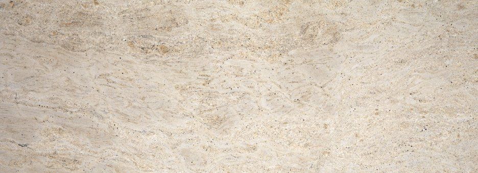 Light beige granite stone surface with fine dark speckles and soft, swirling mineral patterns.