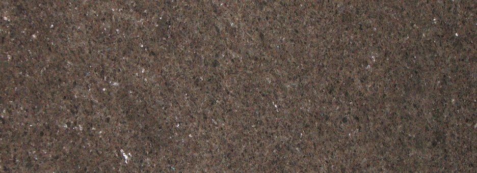 A close-up of dark brown, textured stone or composite surface with small, speckled light-colored flecks throughout.