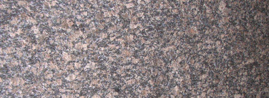 A close-up of a polished brown and gray granite stone surface with a speckled, mottled texture.